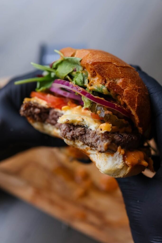 Close-up of a gourmet cheeseburger with toppings held by gloved hand.